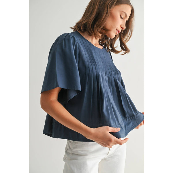 Woman wearing a blue blouse and white pants on a light gray background
