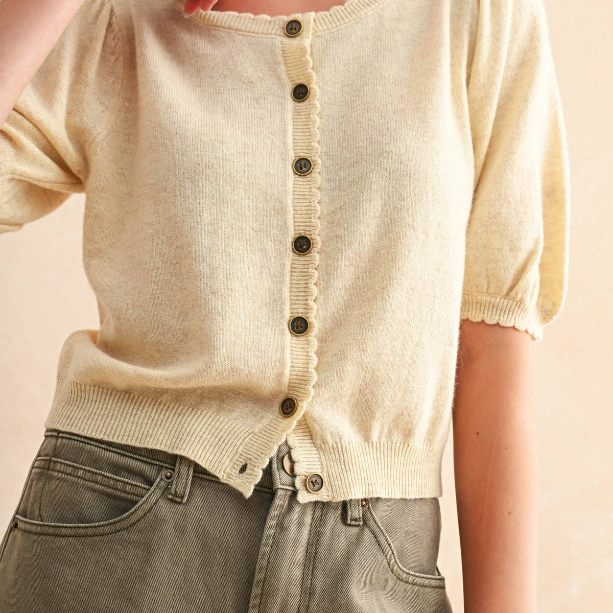 Person wearing a beige knit cardigan with black buttons on a plain background