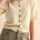 Person wearing a beige knit cardigan with black buttons on a plain background