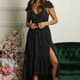 Woman wearing a black polka dot dress with a slit, standing in front of a floral arrangement and green velvet chair.