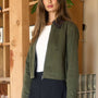 Woman wearing a green jacket over a white top and black skirt in front of a wooden bookshelf.