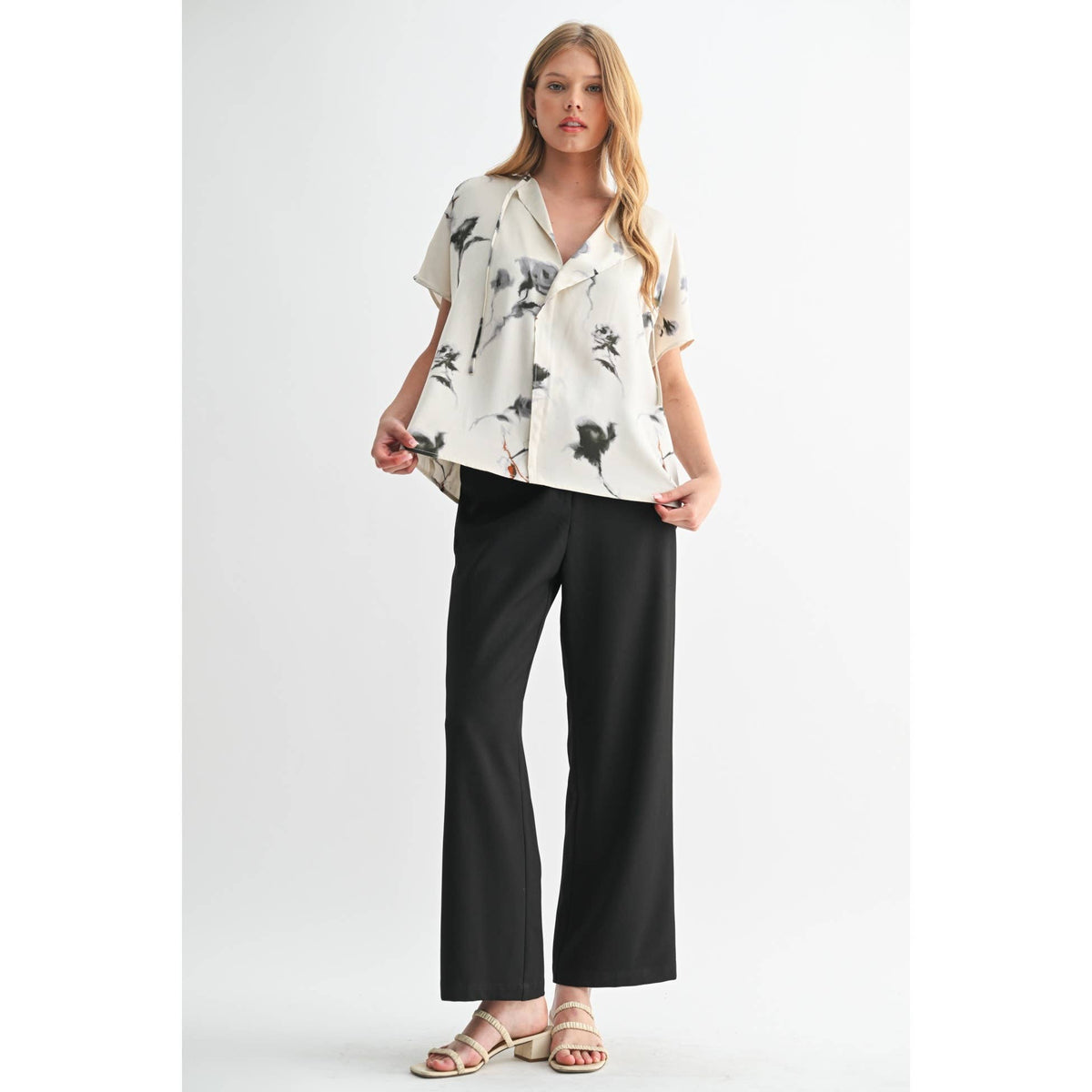 Woman wearing a white blouse with black floral patterns and black pants on a light gray background
