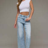 Woman wearing a white crop top and light blue jeans against a neutral background