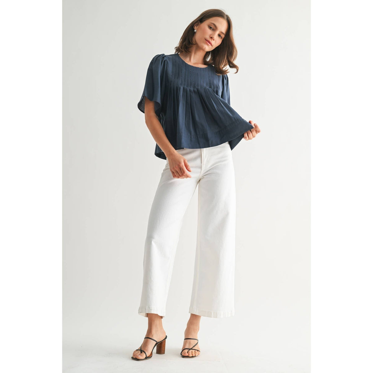 Woman wearing a blue top and white pants on a plain background