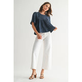 Woman wearing a blue top and white pants on a plain background