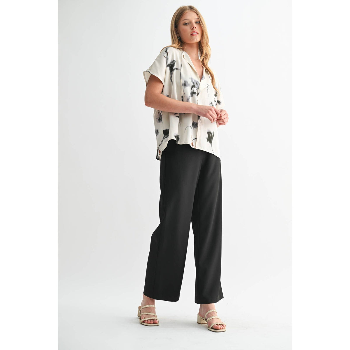 Woman wearing a white blouse with black patterns and black wide-leg pants on a white background
