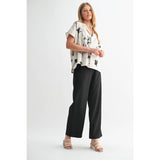 Woman wearing a white blouse with black patterns and black wide-leg pants on a white background