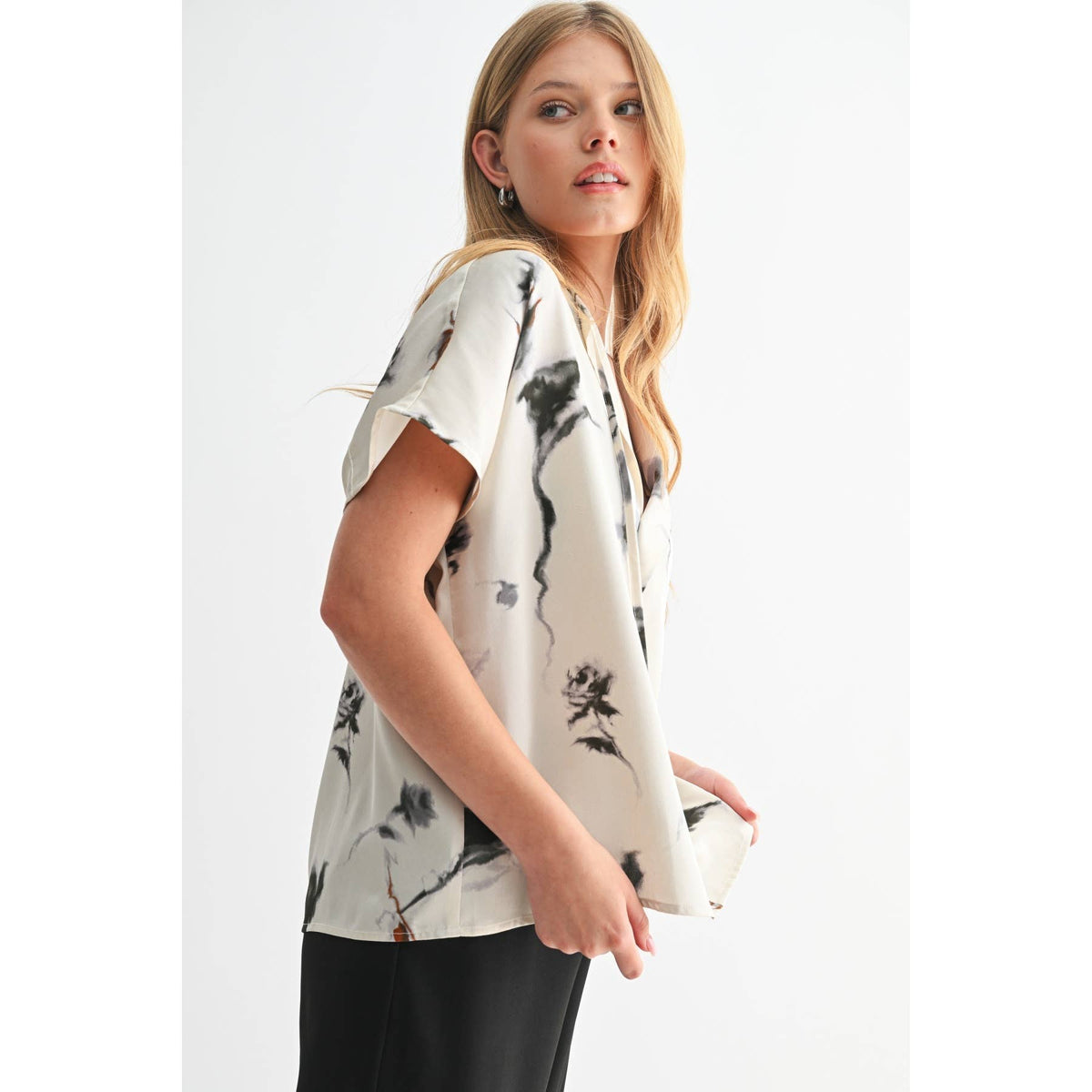 Woman wearing a white blouse with black floral patterns on a plain background