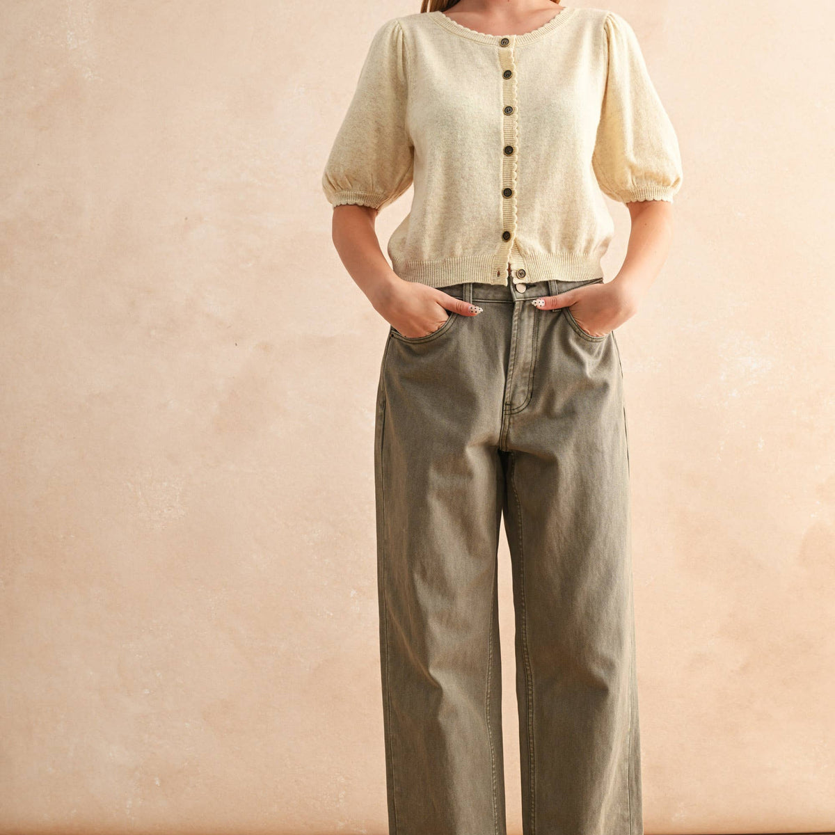 Woman wearing a light-colored blouse and olive green pants against a beige background