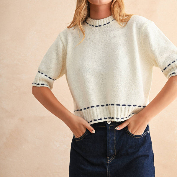 Woman wearing a white sweater with black trim and a dark denim skirt on a beige background