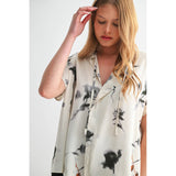 Woman wearing a sleeveless blouse with black floral pattern on a white background