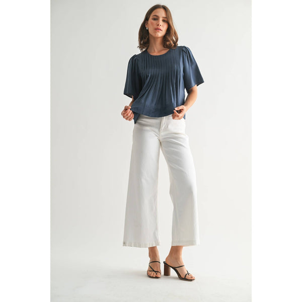 Woman wearing a blue top and white pants on a plain background
