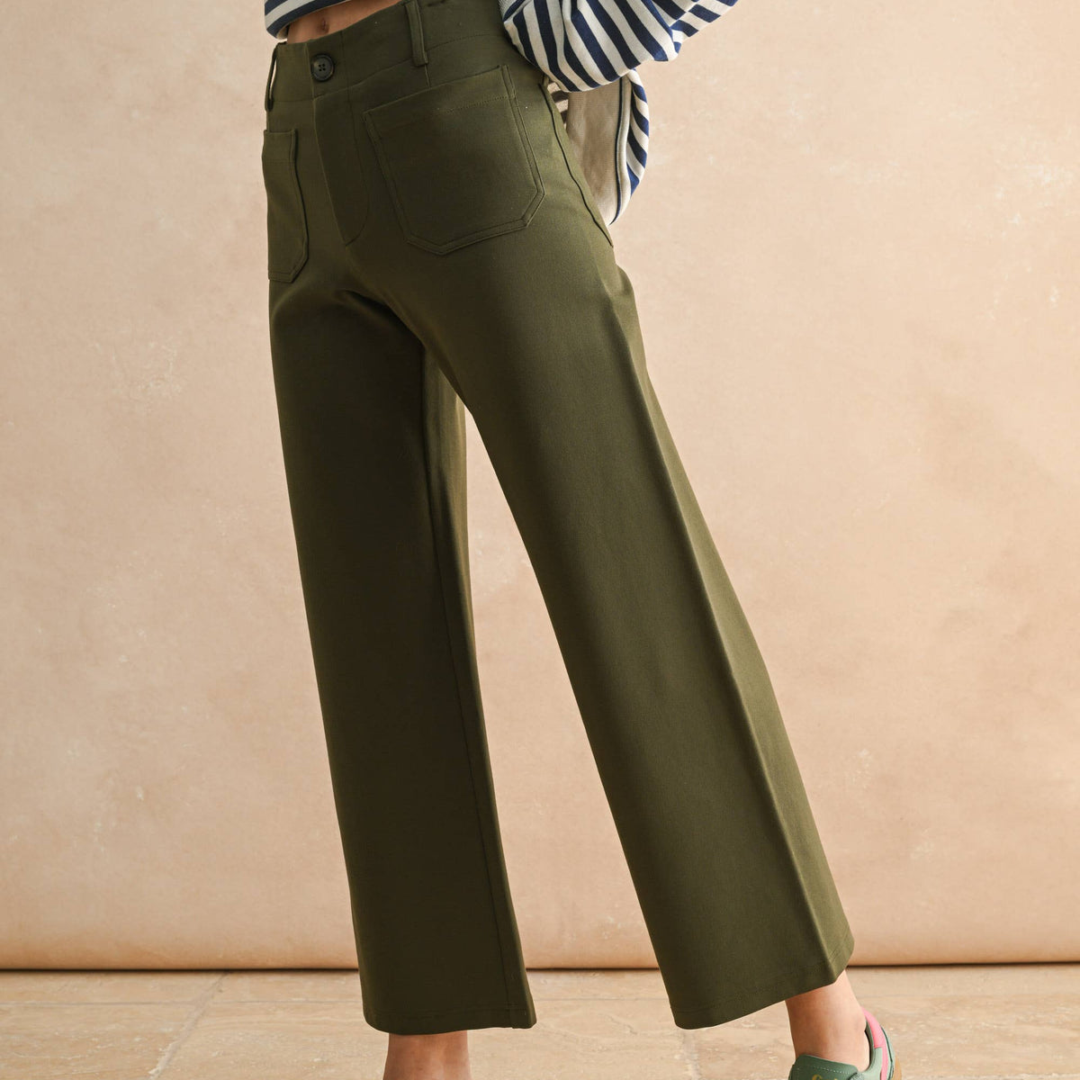 Person wearing green pants and striped shirt against a beige background