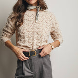 Woman wearing a beige lace sweater and gray pants with a plain background