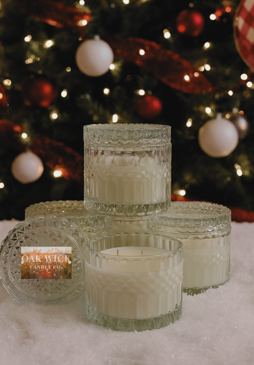 Set of glass candles with decorative lids in front of a Christmas tree.