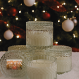Set of glass candles with decorative lids in front of a Christmas tree.