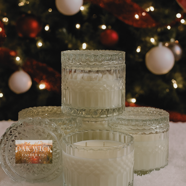Set of glass candles with decorative lids in front of a Christmas tree.