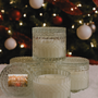 Set of glass candles with decorative lids in front of a Christmas tree.