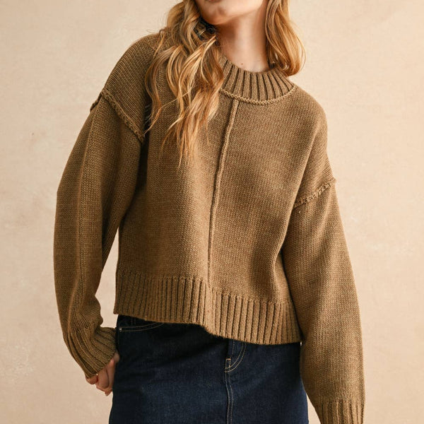 Woman wearing a brown sweater and denim skirt against a beige background
