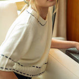 Woman wearing a white sweater with black trim is sitting on a couch.