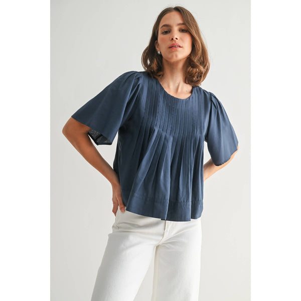 Woman wearing a blue blouse and white pants against a light background
