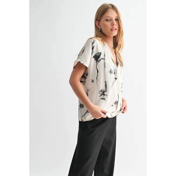 Woman wearing a white blouse with black abstract patterns and black pants on a white background