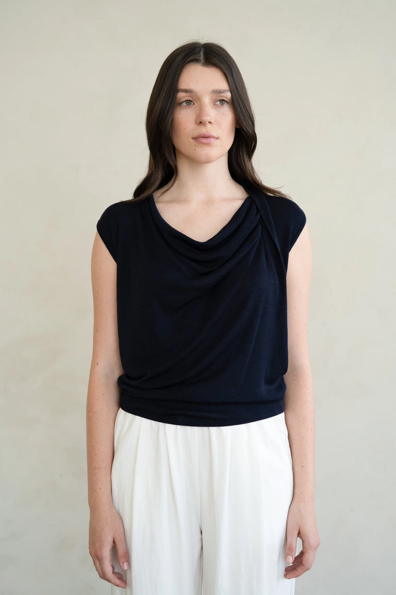Woman wearing a black sleeveless top and white pants against a neutral background