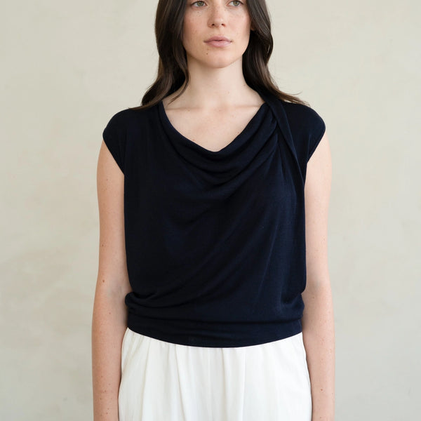 Woman wearing a black sleeveless top and white pants against a neutral background