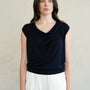 Woman wearing a black sleeveless top and white pants against a neutral background