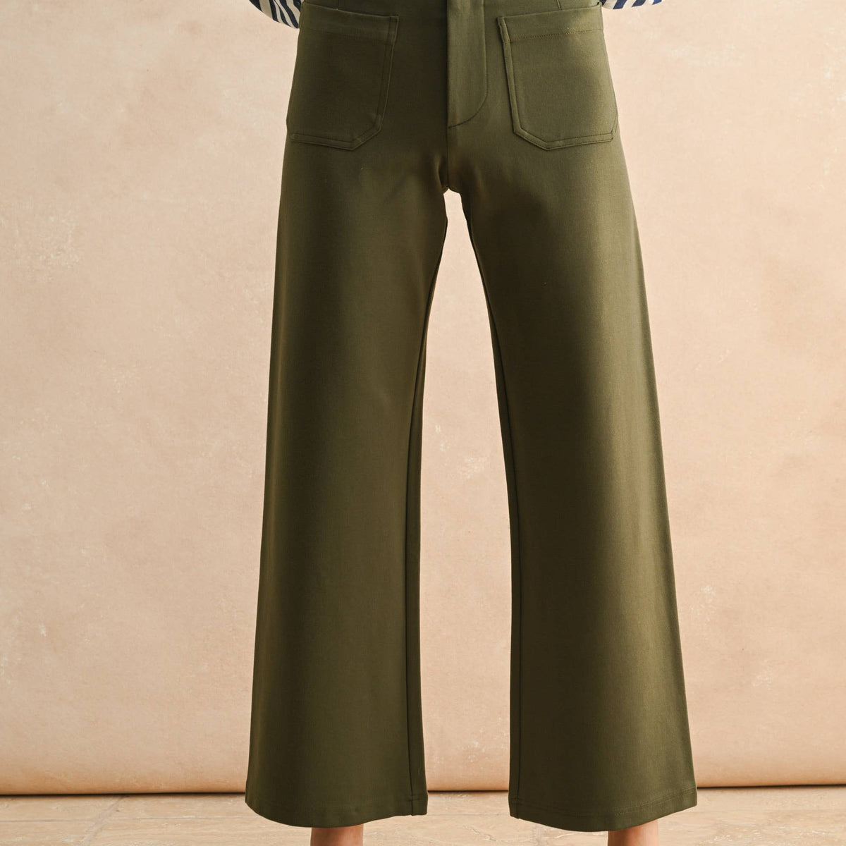 Person wearing green wide-leg pants and a striped shirt against a beige background