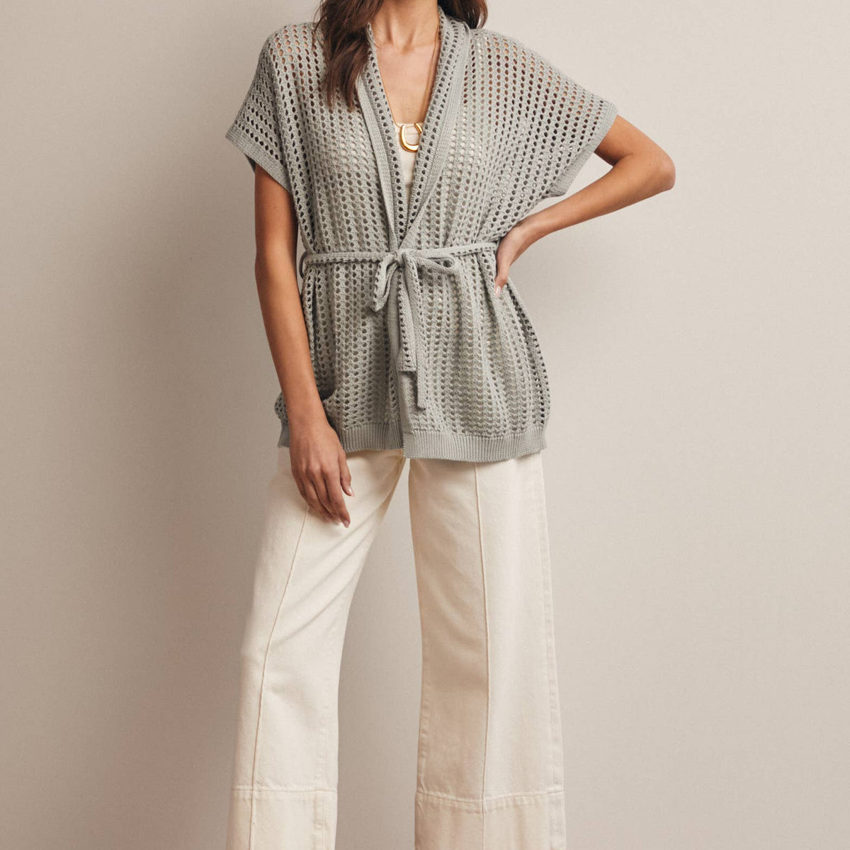 Woman wearing a Sage knit Cardigan with open knit and waist tie, wearing white capri wide leg pants