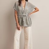 Woman wearing a Sage knit Cardigan with open knit and waist tie, wearing white capri wide leg pants