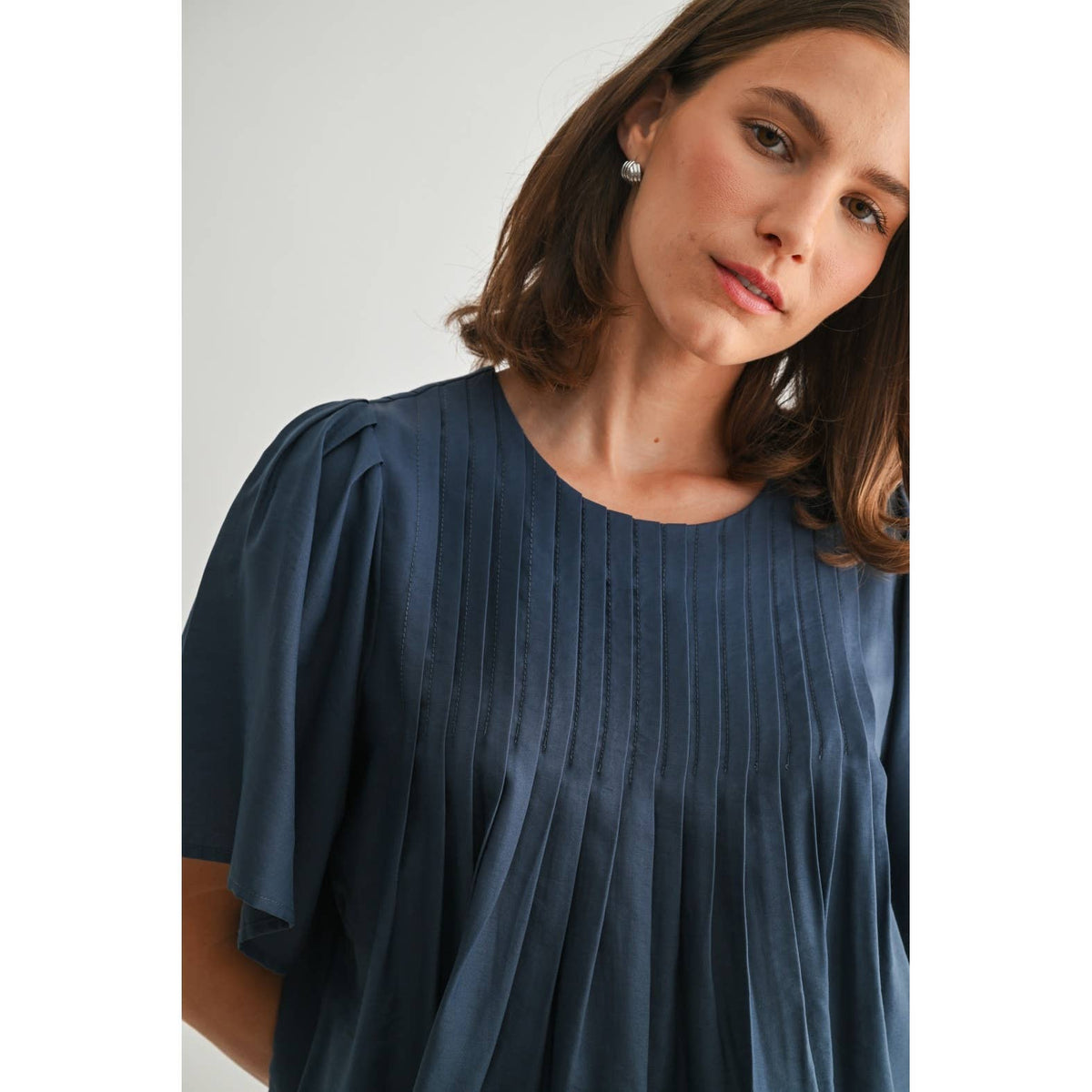Woman wearing a blue pleated dress against a plain background