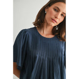 Woman wearing a blue pleated dress against a plain background